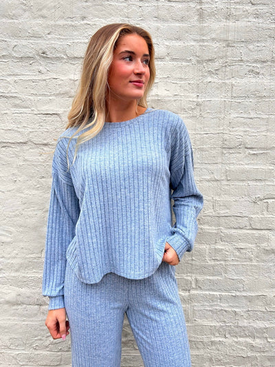 Woman wearing a light blue textured outfit against a gray brick wall.